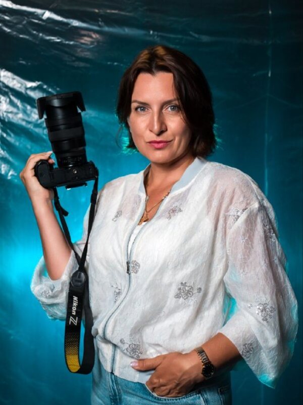 Женщина-фотограф в белой рубашке с камерой Nikon в руке на фоне голубой плёнки